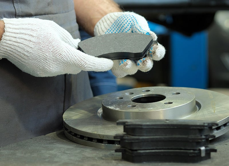 Gloved hands holding brake pad over a brake rotor